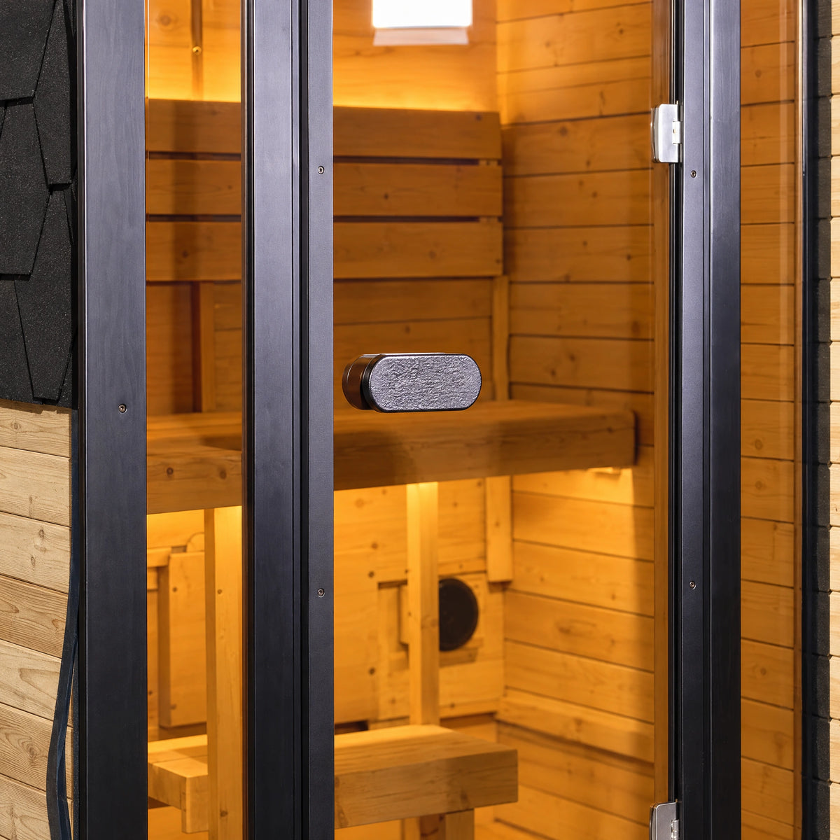 Close view of the compact oval grey pull beside the sauna’s dark door frame and glass.