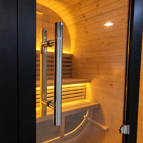 Vertical metal door handle beside the dark frame of the sauna glass front.